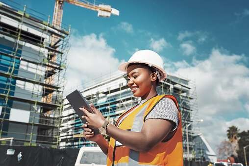 A site engineer in a hard hat smiling at a tablet in front of scaffolding
